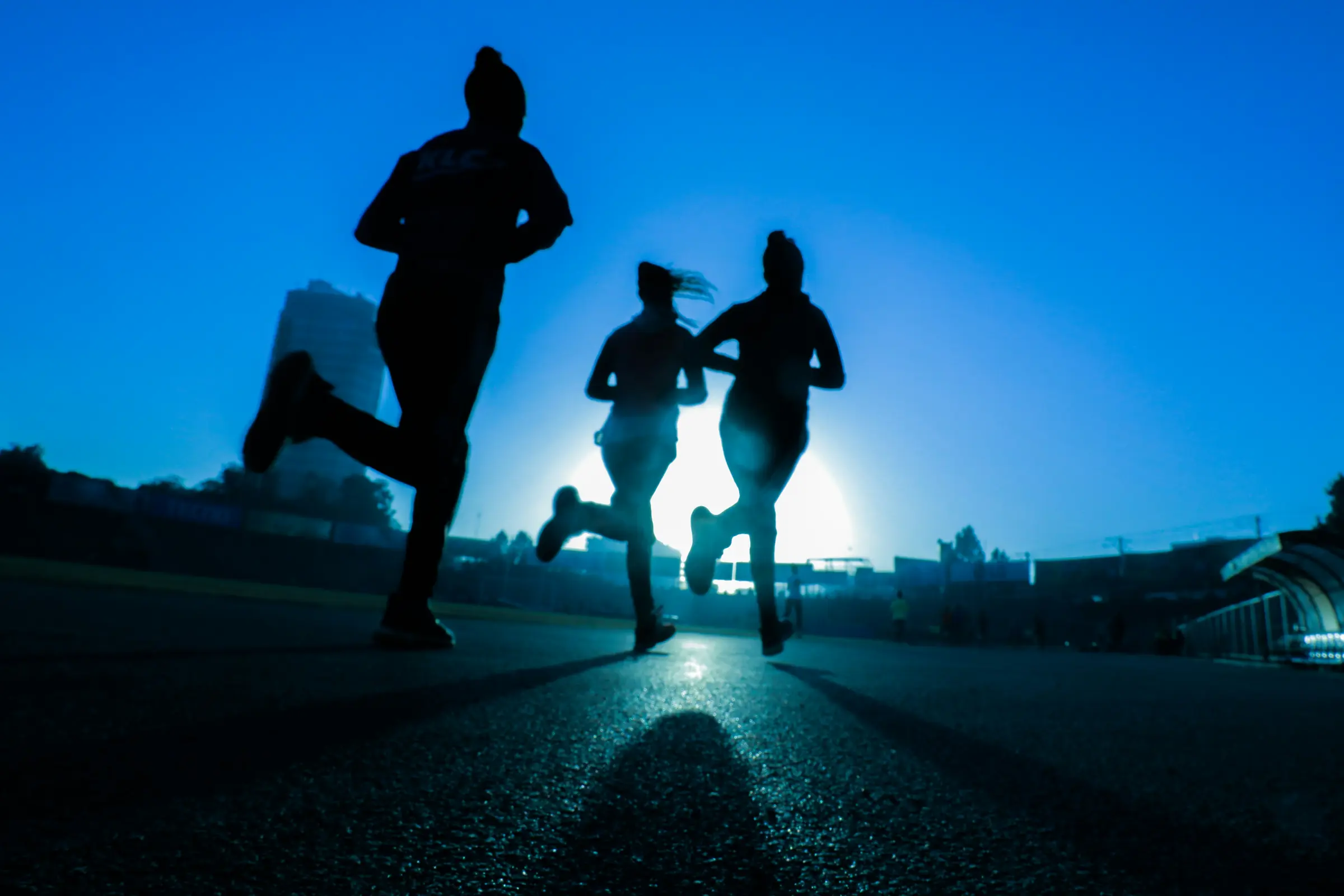 Silhouetted runners moving across a track at sunrise