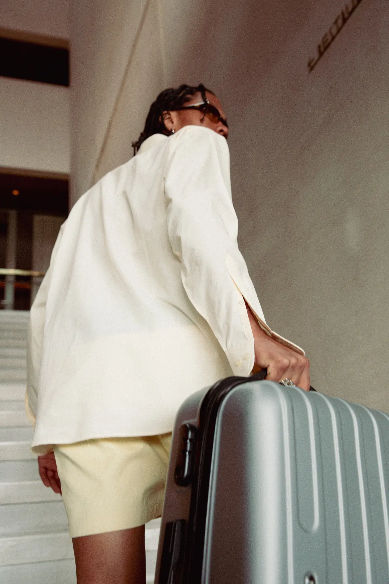 Traveler in a white jacket carrying a silver suitcase up stairs